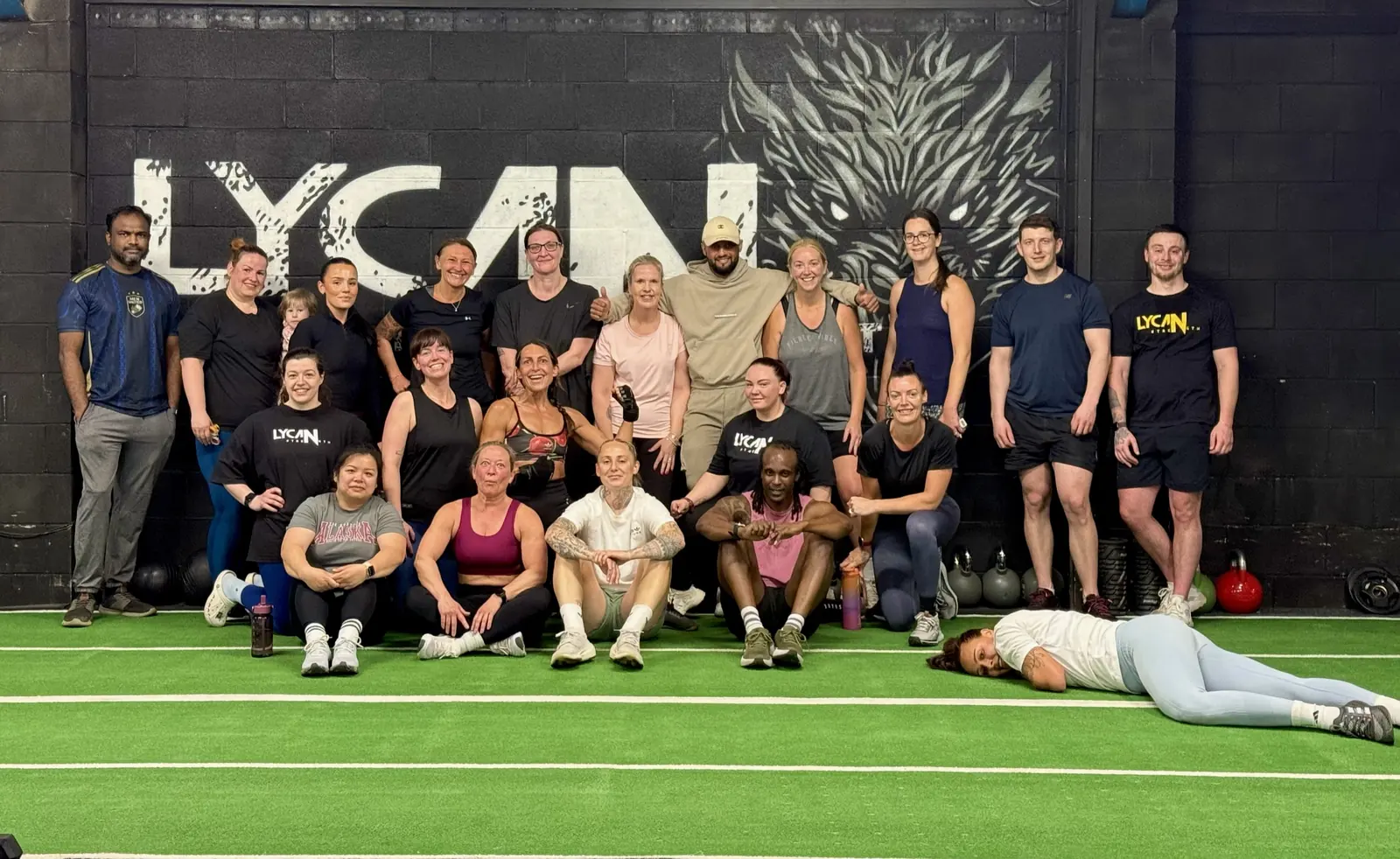 Members sitting on the turf in front of the Lycan wall after a class